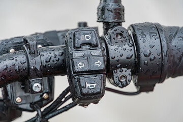Close-up of wet postal electric bicycle handlebars, with brake lever and gear shift visible, under diffused lighting in outdoor setting