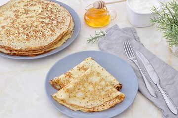 Thin pancakes on a plate, next to honey and sour cream.