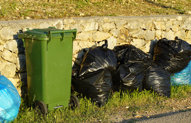 Waste in plastic bags and a plastic bin on the street waiting to be collected