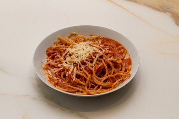 A white ceramic plate with spaghetti with tomato sauce and grated cheese on a marble table