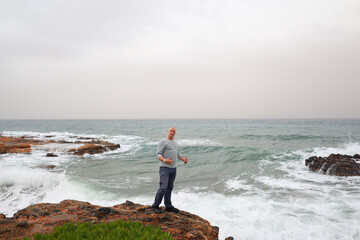 Thoughtful traveler enjoying ocean view on a cloudy day, standing on rugged seaside cliff.
