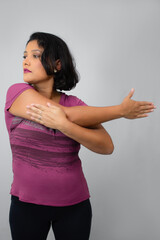 Beautiful, serious woman stretching out her arm. Ideal for home workout, exercising, warm-up and fitness classes. Neutral gray background with copy space.