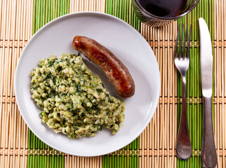 Fried stick of pork frankfurter sausage is garnished with pearl barley porridge with spinach....