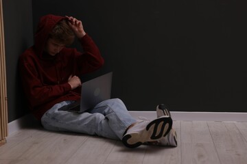 Cyber bullying. Upset teenage boy with laptop on floor indoors. Space for text