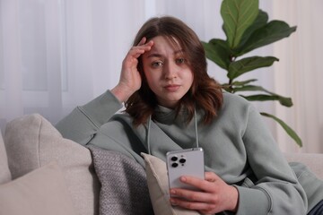 Cyber bullying. Upset teenage girl with smartphone on sofa at home