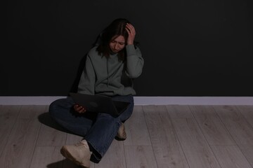 Cyber bullying. Upset teenage girl with laptop on floor indoors. Space for text