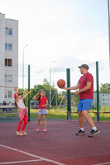 The father teaches the girls how to play basketball on the city playground