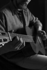 Obraz premium Man playing guitar on dark background, focus on hand. Black and white effect