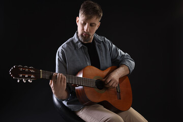 Obraz premium Man playing guitar on chair against black background