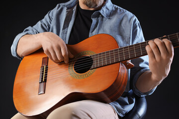 Man playing guitar on black background, closeup