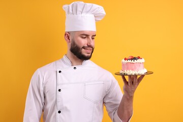 Happy confectioner in uniform holding cake with berries on orange background