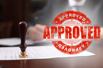 Man working with document at table and red stamp Approved