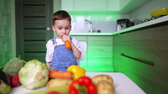 Cute kid eating a carrot looks at the diversity of vegetables. Lively baby picks another carrot. Healthy lifestyle.