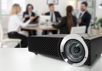 Modern video projector on white table and people working in conference room, selective focus