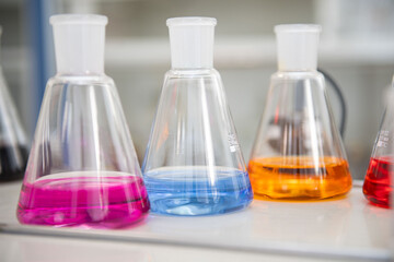 Three conical flasks filled with vibrant liquids are shown in close-up. The bright hues create a...
