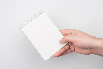 Obraz premium A hand holding a thin, unbound white notebook with lines, partially visible against a neutral backdrop Soft lighting suggests an indoor setting The style is candid and focused on action