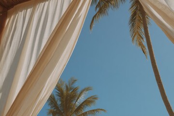 Cozy beach cabana with flowing white linen curtains offering a serene view of swaying palm trees and clear blue skies at sunset