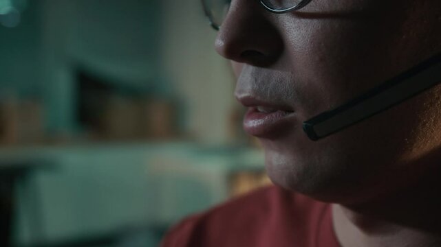 Extreme close-up of lower face, mouth and cleanly shaven chin of anonymous young male scam call center employee wearing headset talking on phone while engaged in bank fraud