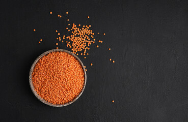 Red lentils in ceramic bowl. Dry orange lentil grains, heap of dal, raw daal, dhal, masoor, Lens culinaris or Lens esculenta on dark background