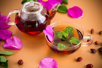 Healing tea with rosehip and mint in transparent cup and teapot on brown background