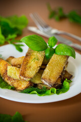 Homemade fried zucchini on a white plate on a brown background