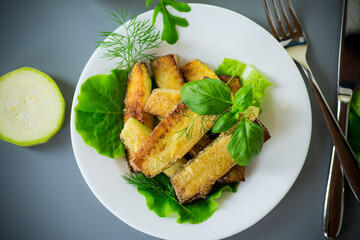 Fried zucchini slices with salad greens on a gray background