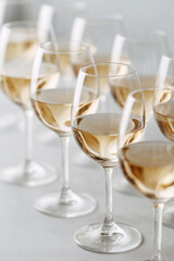 Close-up of multiple wine glasses filled with chilled white wine, arranged in soft focus on a light background