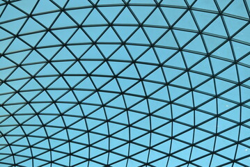 Toit géométrique en verre sous un ciel bleu.