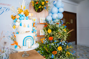 A multi tiered cake with blue, orange, and gold decorations, surrounded by floral arrangements and...