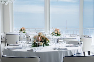 Sophisticated dining space with white tablecloths, floral centerpieces, and large windows showcasing the Tyrrhenian Sea under a clear blue sky.