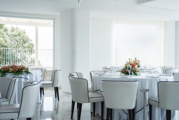 Refined dining space in Amalfi, Italy, featuring white walls, marble flooring, round tables with floral decor, and large windows with partial greenery views.