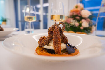Crispy octopus on cheese and tomato, garnished with purple basil. Two wine glasses and flowers in a fine dining setting with Amalfi evening views.