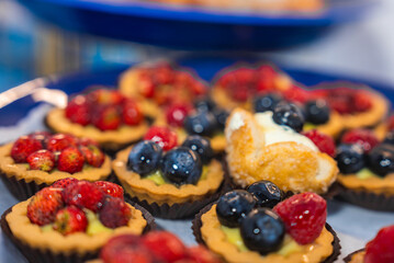 A close up view of fruit tarts with strawberries, blueberries, raspberries, and a cream filled pastry on a blue plate, showcasing Amalfi's culinary style.