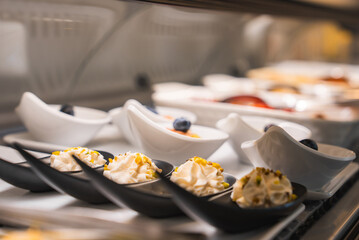 Small black spoons with whipped cream and pistachios in the foreground, with white bowls of desserts and blueberries in a refined Amalfi setting.