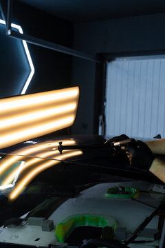 PDR Accurate paintless car dent removal. PDR technician holds a specialized hammer against a reflection light board to check dent correction on the hood.