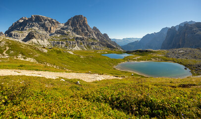 Gentle slopes with dense grass descend to mountain area Laghi dei piani with emerald clear water,...