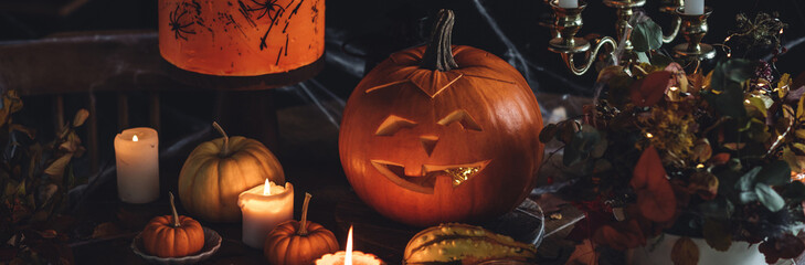 Elegant beautiful Halloween party table decor. Burning candled in vintage chandelier, handmade cake, meringue ghosts, handmade jack-o-lantern. Dark background wooden old furniture, spider web banner