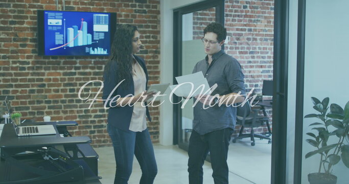 Heart month text banner against diverse male and female office colleagues discussing at office - Powered by Adobe