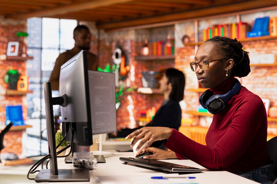 Programmer in startup office using large language model to get help with coding project. African american worker interacting with AI LLM chatbot PC GPT software on PC in software development workplace