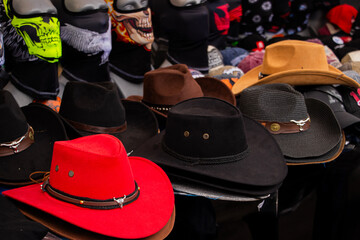 Bright red cowboy hat with metal bull detail displayed among black hats on a dark market stall...