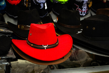 Bright red cowboy hat with metal bull detail displayed among black hats on a dark market stall...