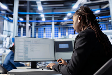 Engineer coding at workstation in solar panel manufacturing plant, developing programs to automate equipment processes. Photovoltaics factory expert writing scripts to optimize robotic operations