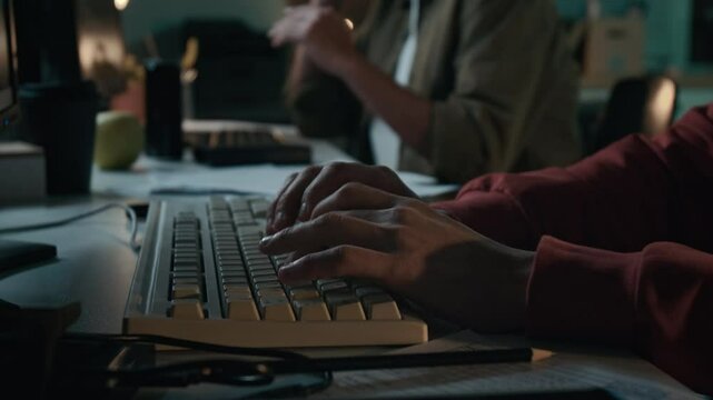 Close-up of hands of anonymous male scam perpetrator typing on computer keyboard while working at fraud call center during phone conversation with target