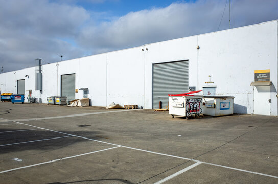 A large, unkempt, and disorganized industrial warehouse with a rear loading area scattered with graffiti-covered commercial waste bins, pallets, and debris in Australia.