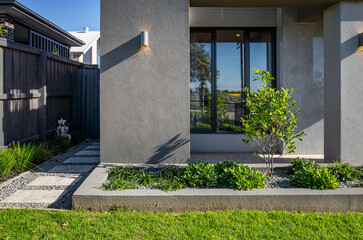 A minimalist front yard in a modern suburban home in Australia, featuring concrete stepping stones,...