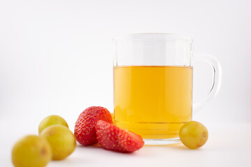 Clear glass mug with golden herbal tea next to a wooden coaster holding fresh strawberries and green grapes. The arrangement suggests a focus on health and nutrition, with elegant presentation.