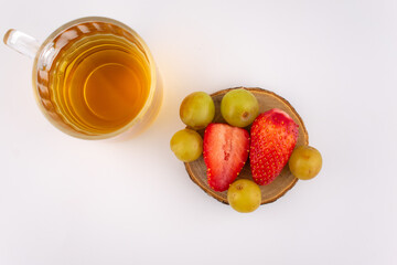Clear glass mug with golden herbal tea next to a wooden coaster holding fresh strawberries and green grapes. The arrangement suggests a focus on health and nutrition, with elegant presentation.