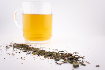 close-up features a clear glass of vibrant green tea, with loose leaves gracefully scattered below, evoking a sense of calm and healthy indulgence. Ideal for wellness, detox, or mindful living content