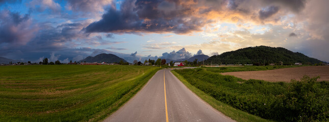 Obraz premium Panoramic View of a Rural Road with Mountains and Dramatic Clouds