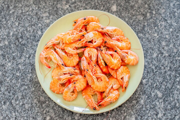 Cooked shrimps are arranged on a light green plate placed on a granite countertop, ready to be enjoyed as a delicious seafood meal or appetizer